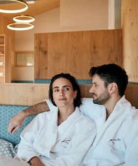 Paar entspannt in Spa-Lounge in weißen Bademänteln mit Wellness-Logo
