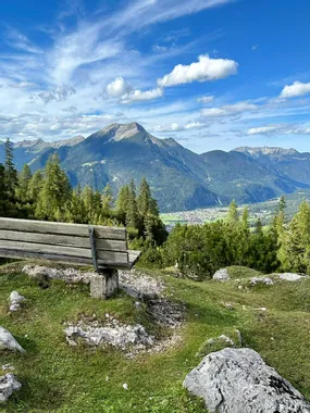 Wooden bench on alpine trail overlooking mountain range and valley under blue sky