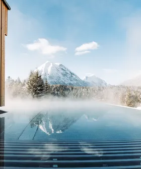 Steam rising from outdoor infinity pool facing snow-covered alpine mountains