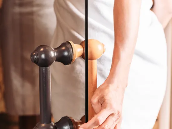 Frau im Handtuch öffnet Glastür zur Sauna mit Holzgriff