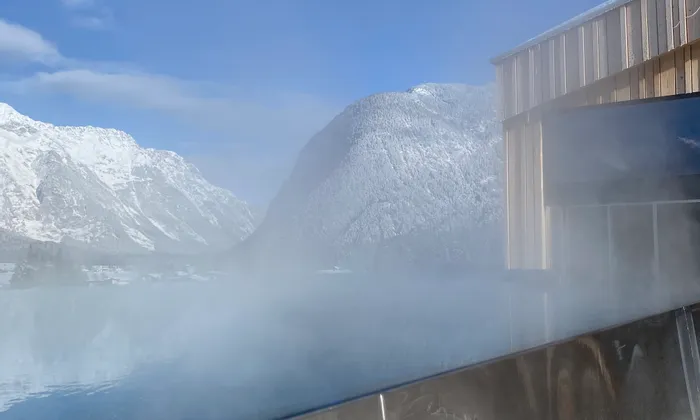 Dampf steigt aus einem Infinity-Pool mit verschneiten Alpen im Hintergrund auf
