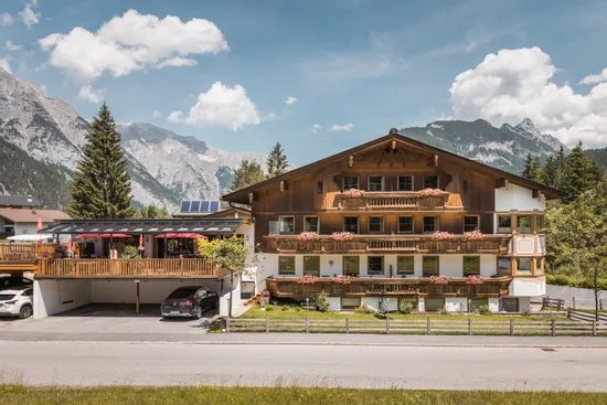 Alpine hotel with flower-decorated balconies and mountain view under blue sky