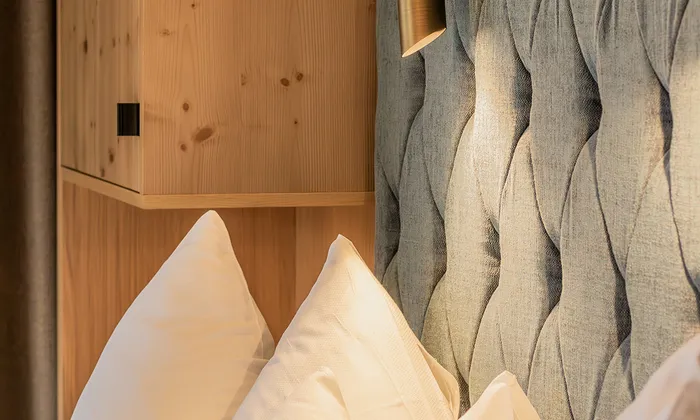 Cozy hotel bed with white pillows, wood paneling, and textured fabric headboard