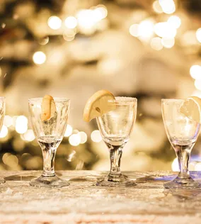 Vier Gläser mit Zitronenscheiben auf schneebedeckter Bar vor festlichen Lichtern