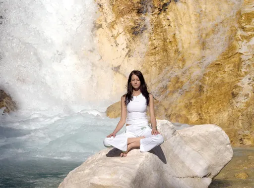 Frau meditiert im Lotussitz auf Felsen nahe Wasserfall in der Natur