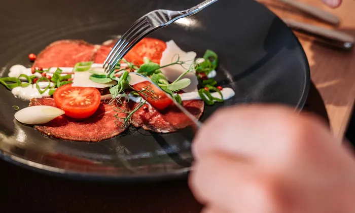 Rinder-Carpaccio mit Cherrytomaten, Grünen und Parmesan auf schwarzem Teller in elegantem Restaurant