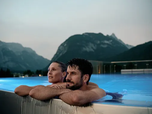 Couple relaxing in rooftop infinity pool with mountain view at dusk