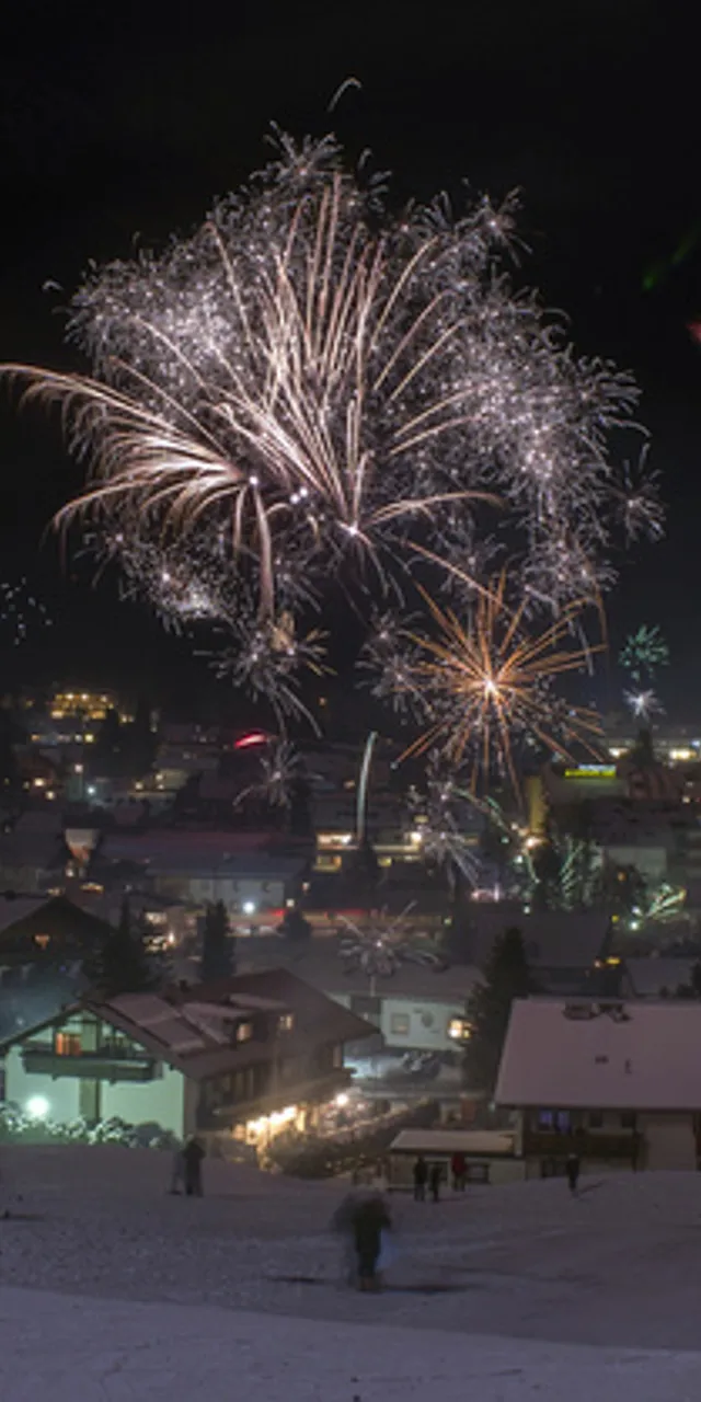 Bunte Feuerwerke erhellen den Nachthimmel über einem verschneiten Alpendorf