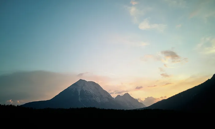 Snow-covered mountain range with forest silhouette at sunset