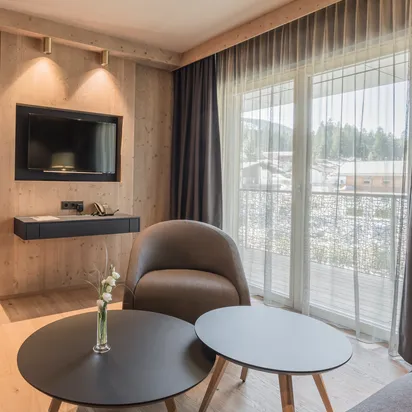 Modern hotel suite with wooden walls, cozy seating area, flat-screen TV, and balcony view