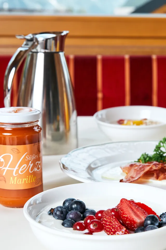 Frühstückstisch mit Joghurt und Beeren, Marillenmarmelade, Speck und einem Glas Sekt