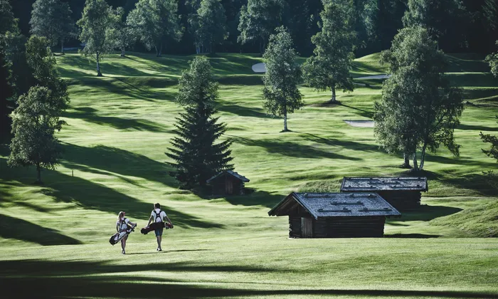 Golfers walking on green fairway with golf bags in scenic mountain course