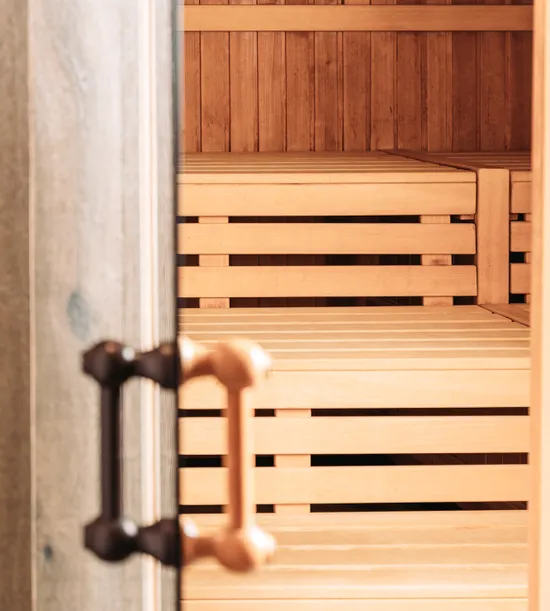 Open wooden sauna door revealing interior with light wood benches