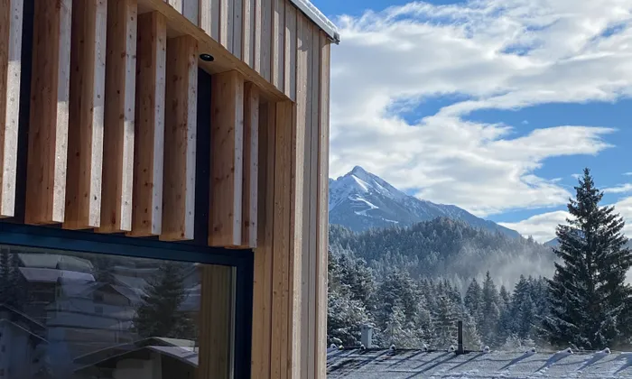 Modernes Holzgebäude mit verschneitem Dach und Bergblick unter klarem blauen Himmel