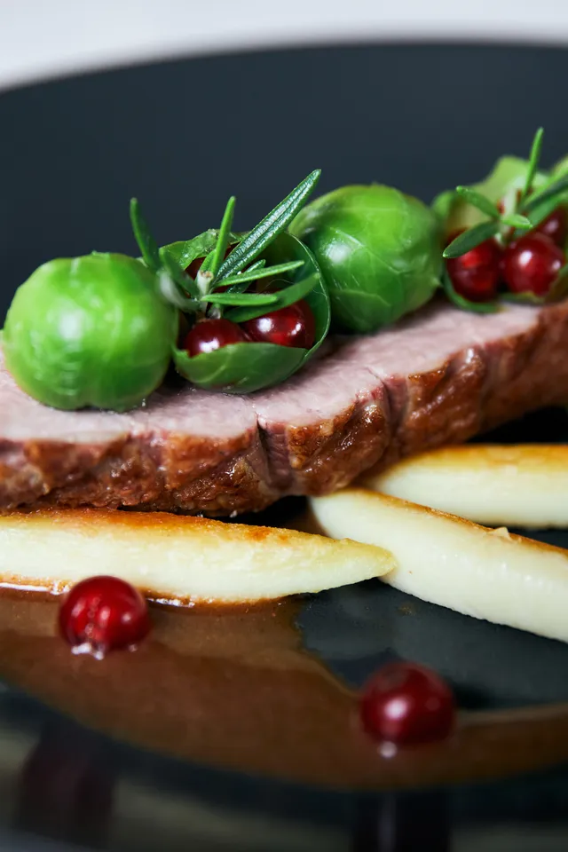 Roast duck breast with Brussels sprouts, red currants, and potato fingers on dark plate