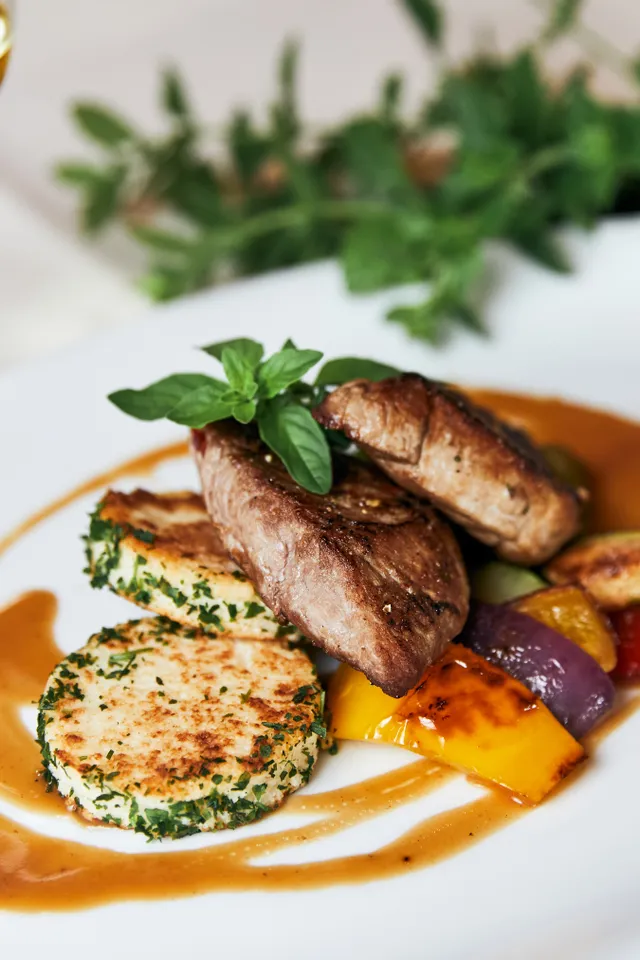 Grilled steak with vegetables, potato cakes and sauce on a white plate, served with white wine