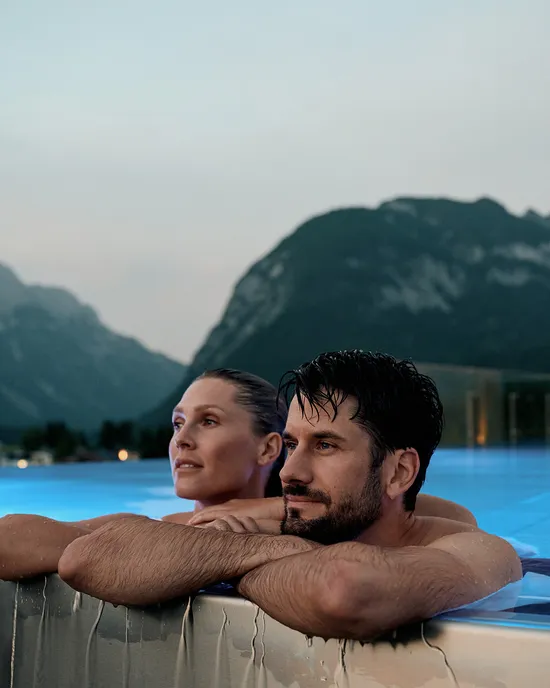 Couple relaxing in rooftop infinity pool with mountain view at dusk