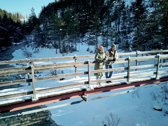 Paar in Winterkleidung auf verschneiter Brücke über Waldbach