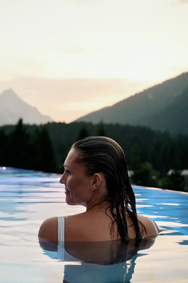 Couple relaxing in infinity pool with mountain view at sunset