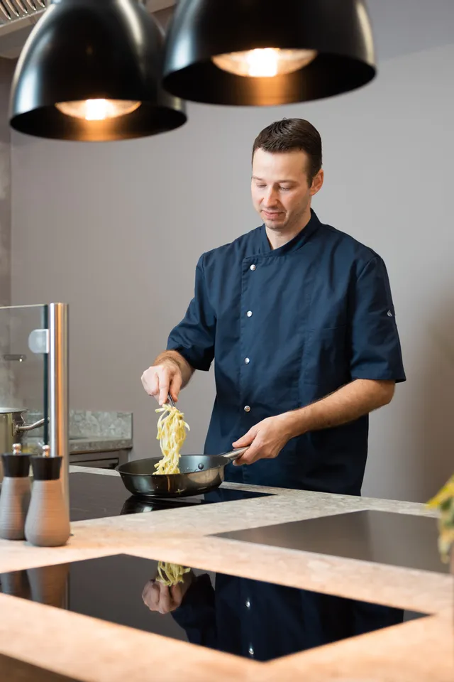 Chef in modern kitchen cooking pasta with vegetables and oils on counter