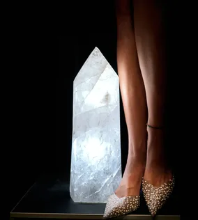 Beine einer Frau in glitzernden High Heels neben großem leuchtendem Quarzkristall