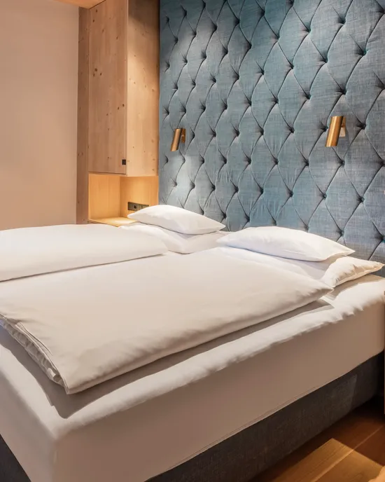 Modernes Hotelzimmer mit Doppelbett, Holzakzenten und gepolsterter blauer Wandverkleidung