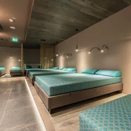Modern spa relaxation room with multiple teal lounge beds and ambient lighting
