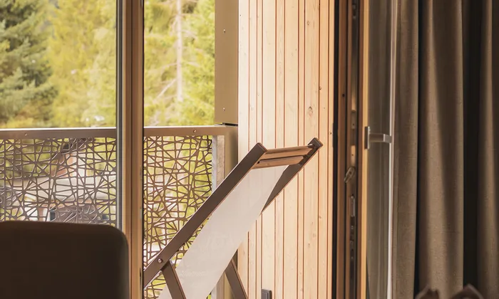 Gemütlicher Hotelbalkon mit Holzliegestuhl und Blick auf Wald und Berge