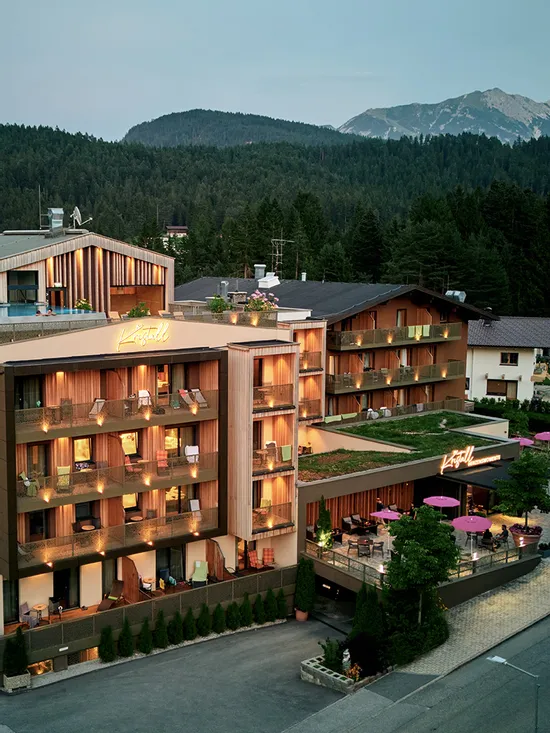 Modernes Alpenhotel mit Balkonen und Dachterrasse umgeben von Bergen und Wald
