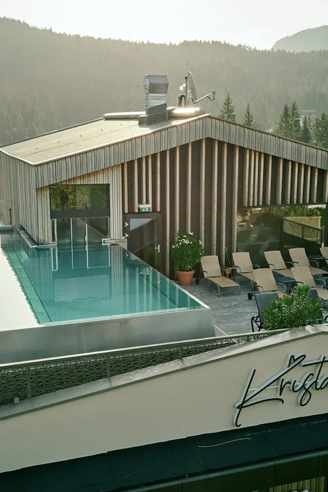 Rooftop infinity pool with mountain view at Hotel Kristall in a forested alpine setting