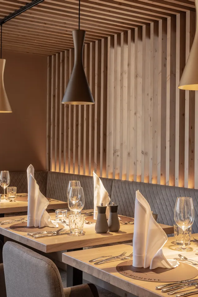 Elegant restaurant interior with wooden panels, set tables, and modern pendant lighting