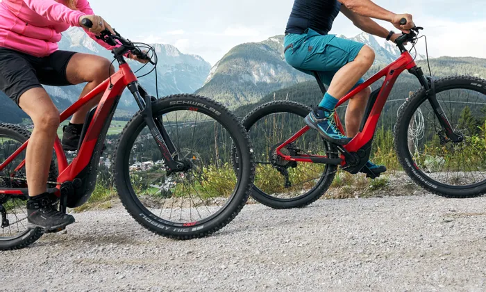 Couple riding red electric mountain bikes on gravel trail with scenic alpine backdrop