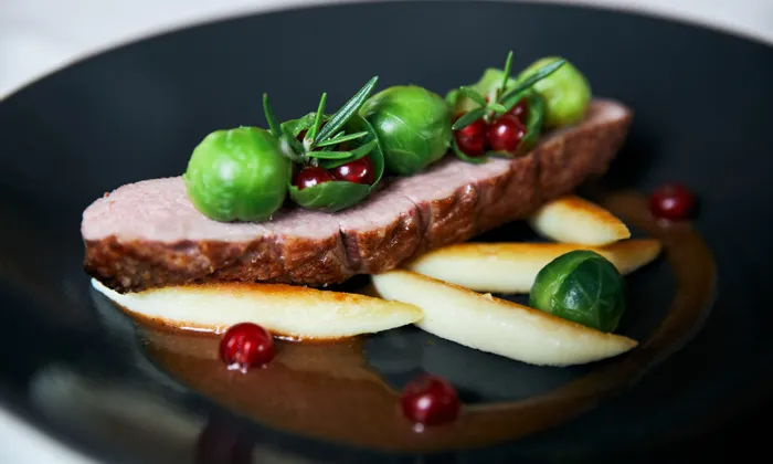 Roast duck breast with Brussels sprouts, red currants, and potato fingers on dark plate
