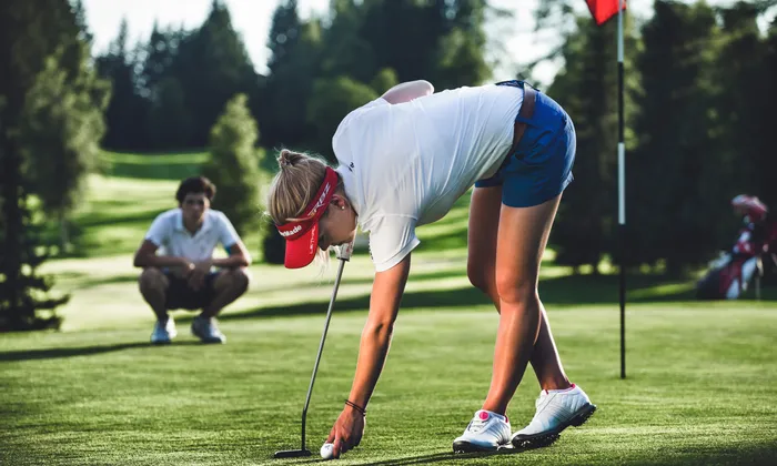Female golfer placing ball on green with putter near hole on sunny golf course