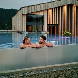 Paar entspannt im Infinity-Pool auf dem Dach eines luxuriösen Alpinresorts mit Holzarchitektur