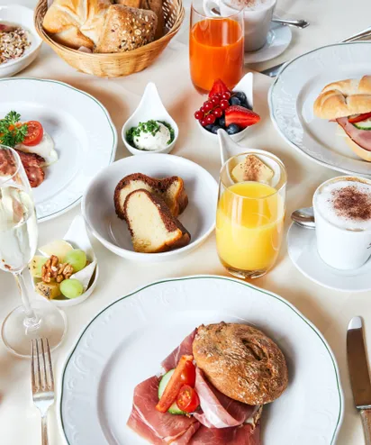 Elegantes europäisches Frühstück mit Aufschnitt, frischem Brot, Obst, Säften, Kaffee und Gebäck auf weißem Tisch