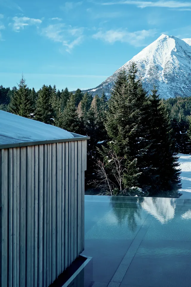 Modernes Spa mit Infinity-Pool und Blick auf verschneite Berge und Kiefernwald