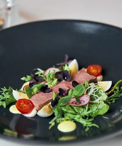 Gourmet beef salad with cherry tomatoes, egg wedges, and mixed greens on black plate