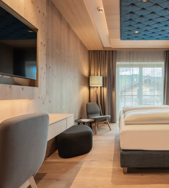 Modern hotel room with wooden furniture, large bed, and quilted blue wall panels