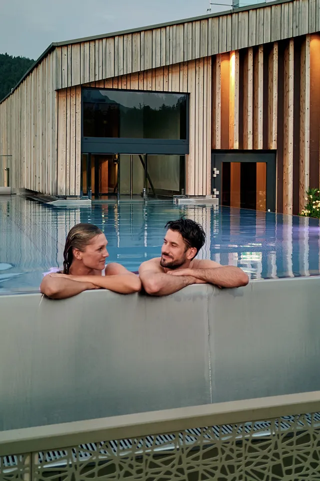Paar entspannt im Infinity-Pool auf dem Dach eines luxuriösen Alpinresorts mit Holzarchitektur