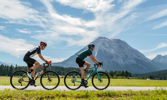 Two cyclists riding road bikes on a scenic trail with mountains in the background
