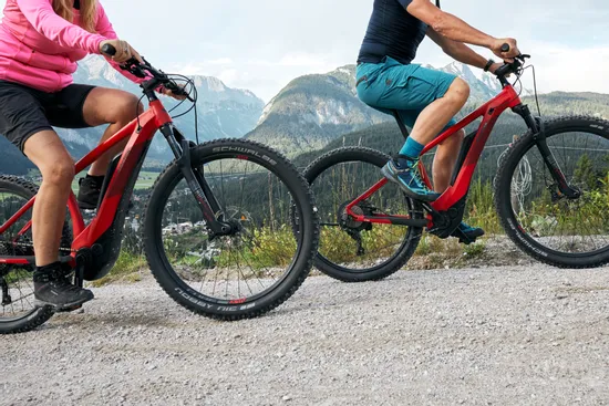Couple riding red electric mountain bikes on gravel trail with scenic alpine backdrop