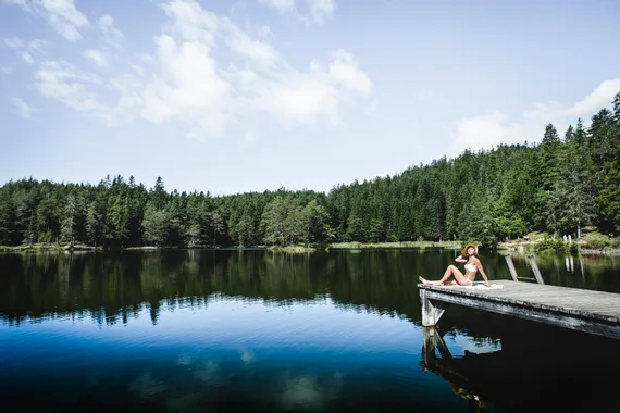 Woman in swimsuit relaxing on wooden dock by forest lake in summer