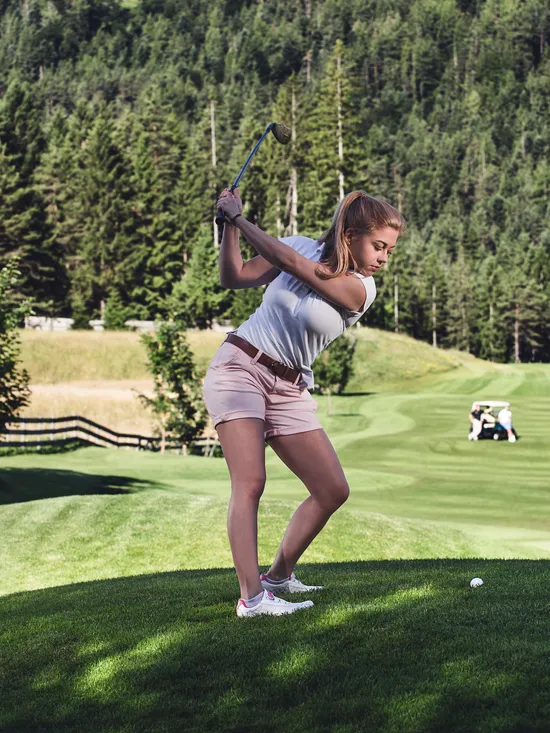 Frau schlägt mit Golfschläger auf malerischem Golfplatz inmitten bewaldeter Hügel