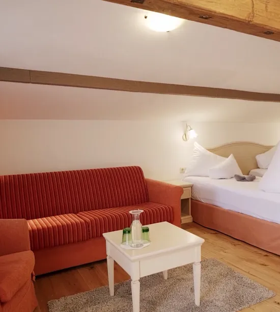 Cozy hotel room with twin beds, red sofa, armchair, wooden floor and sloped ceiling