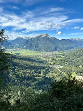 Panoramablick auf die Bayerischen Alpen mit bewaldetem Tal und Dorf unter blauem Himmel