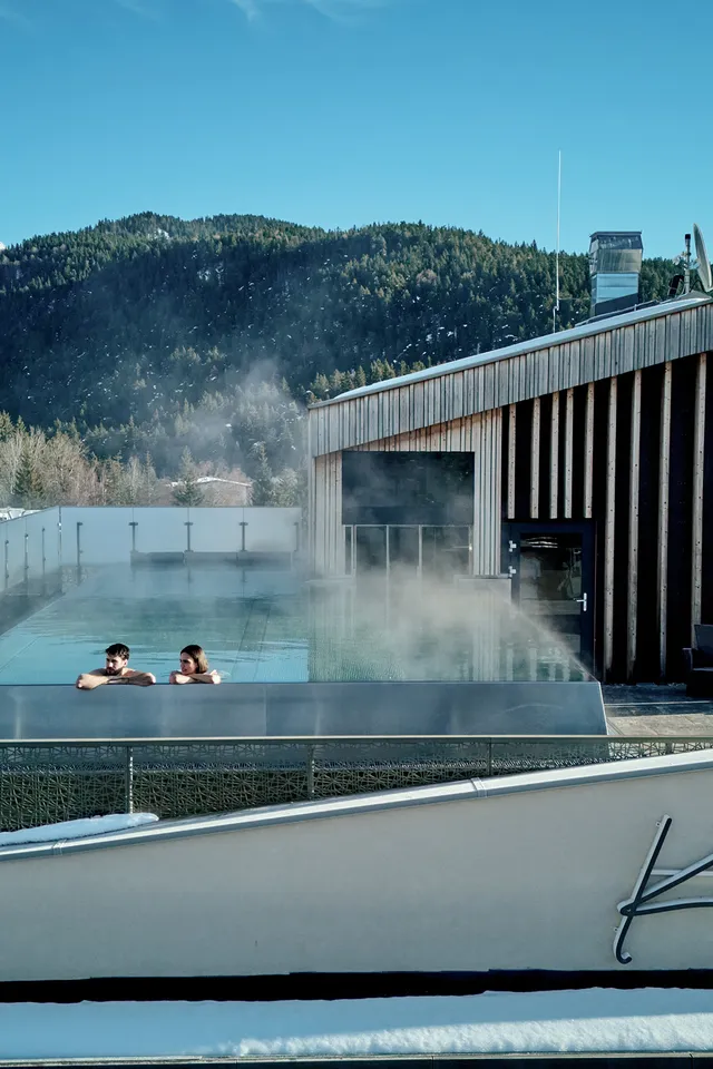 Paar entspannt im Infinity-Pool auf dem Dach des Hotels Kristall in verschneiter Alpenkulisse