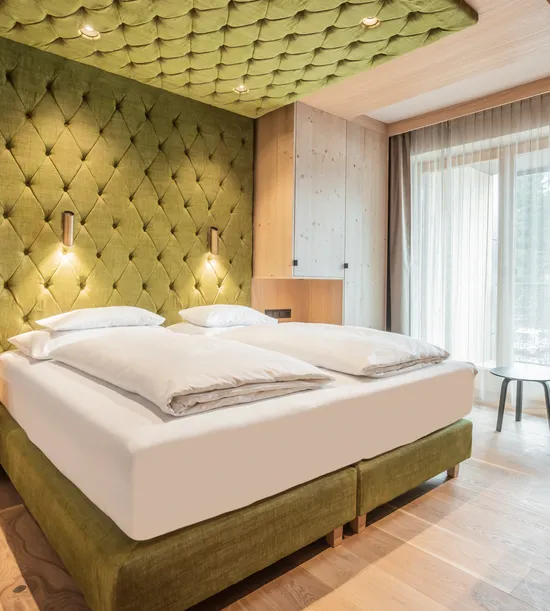 Modern hotel room with green upholstered bed, wood furnishings, and floor-to-ceiling window