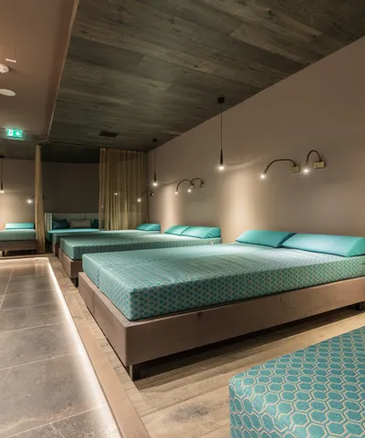Moderner Spa-Ruhebereich mit mehreren türkisfarbenen Liegebetten und stimmungsvoller Beleuchtung