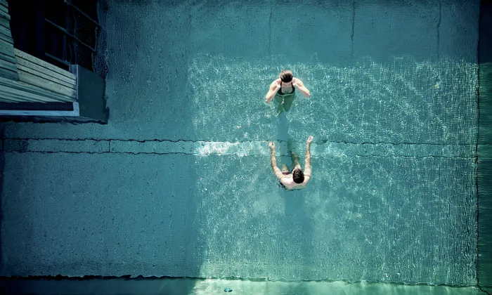 Zwei Personen entspannen sich in einem klaren türkisfarbenen Schwimmbecken von oben gesehen